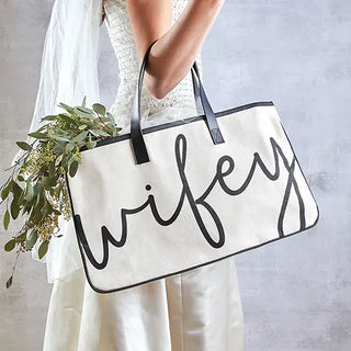 Person holding a tote bag with 'wifey' text and a bouquet of flowers.