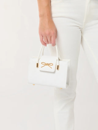 White handbag with gold accents held by a person wearing white pants on a light background