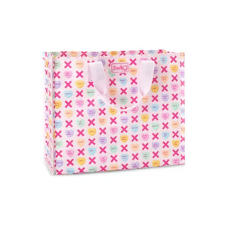 A pink gift bag with a repeating pattern of pastel candy hearts and pink X's, featuring light pink handles and a pink Swig logo patch on the front, set against a plain white background.