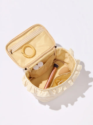 Beige jewelry case with ruffled edge containing jewelry on a white background