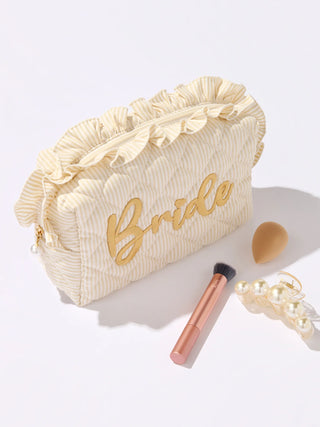 Beige makeup bag with 'Bride' text, brush, and pearl necklace on a white background