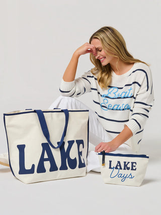 Woman holding a tote bag and pouch with 'Lake' text, wearing a striped sweater.