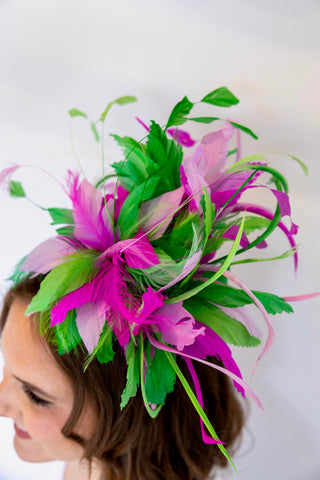 Woman wearing a decorative headpiece with pink and green feathers on a white background