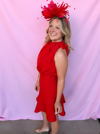 Woman wearing a red dress and large feathered headpiece against a pink background