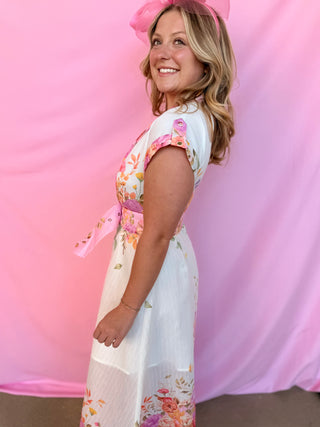 Woman wearing a floral dress with a pink ribbon against a pink background