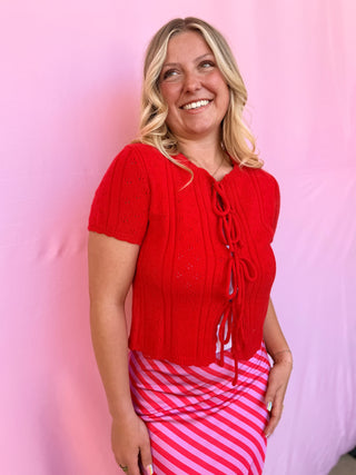 Woman wearing a red knitted top with a pink and white striped skirt against a pink background