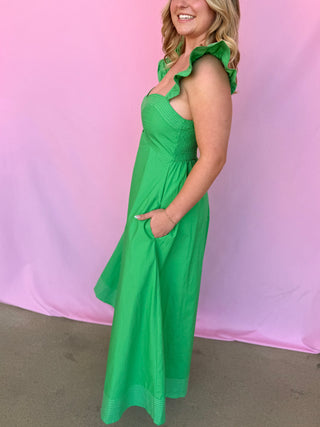 Woman wearing a green dress with ruffled straps against a pink background