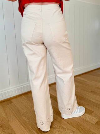 Person wearing a red top and white pants standing in a room with wooden flooring and white walls.