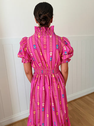 Person wearing a pink dress with intricate patterns in a room with white walls and wooden flooring.