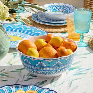 Decorative bowl with fruits on a table with floral tablecloth and glasses.