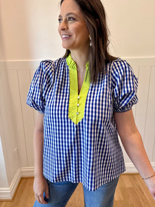 Woman wearing a blue and white checkered blouse with yellow trim in a room.