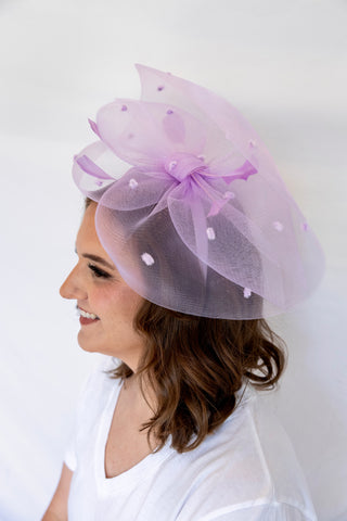 Woman wearing a light purple fascinator with a bow on a white background