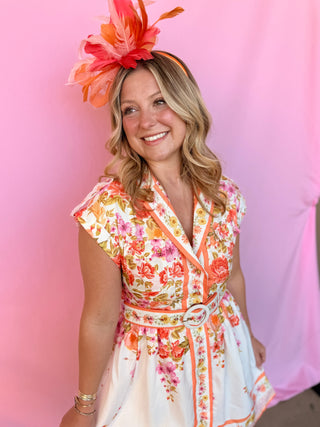 Woman wearing a floral dress and large decorative headpiece against a pink background