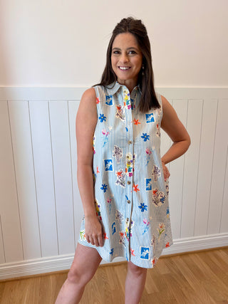 Woman wearing a patterned dress standing against a white paneled wall.
