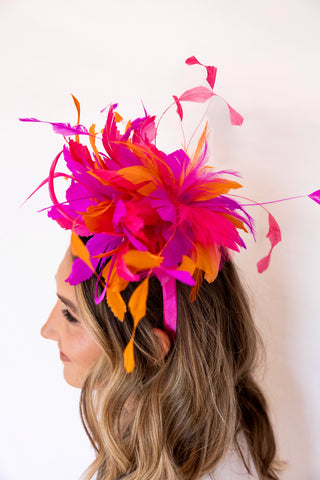 Woman wearing a vibrant pink and orange feathered headpiece against a white background