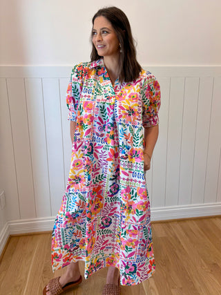 Woman wearing a colorful floral dress standing in a room with wooden flooring and white paneled walls.