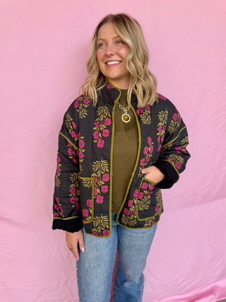 Woman wearing a floral embroidered jacket against a pink background