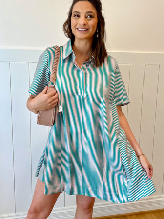 Woman wearing a striped dress holding a handbag against a white wall.