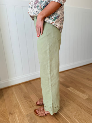 Person wearing light green pants with lace trim on a wooden floor.