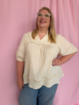 Woman wearing a beige blouse and blue jeans against a pink background