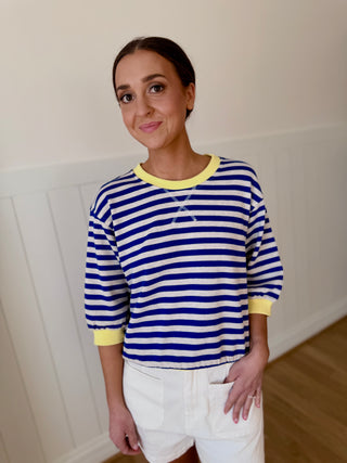 Woman wearing a blue and white striped sweater with yellow trim indoors.