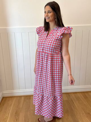 Woman wearing a red and white checkered dress standing against a white paneled wall.