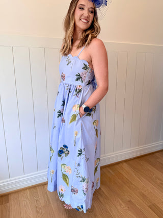 Woman wearing a light blue floral dress standing against a white paneled wall.