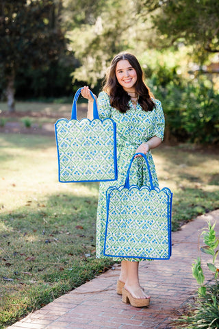 Woman holding two large patterned bags outdoors on a path with greenery.