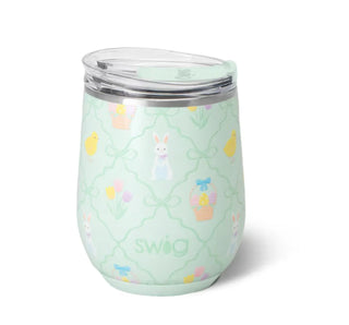 A mint green insulated tumbler with a clear lid, decorated with a pastel Easter pattern featuring bunnies, chicks, baskets, and tulips. The brand name 'swig' is printed near the bottom.