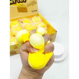 Hand holding a yellow squishy toy with a box of similar toys in the background.