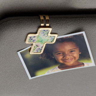 Gold cross pendant with floral design on a gray surface next to a photo of a smiling child