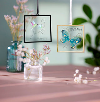 Decorative wall hangings with floral and butterfly designs on a table with flowers and a vase.