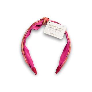Pink headband with a floral pattern on a white background, featuring a visible brand tag.