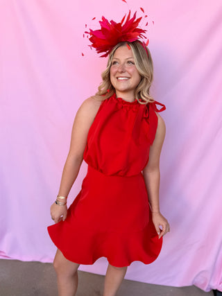 Woman wearing a red dress and large red feathered headpiece against a pink background