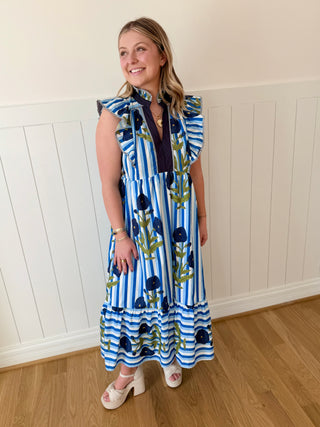 Woman wearing a blue and white striped dress with floral patterns against a white paneled wall.
