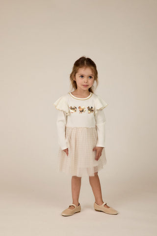 Young girl wearing a white top with ruffled sleeves and a beige skirt on a plain background