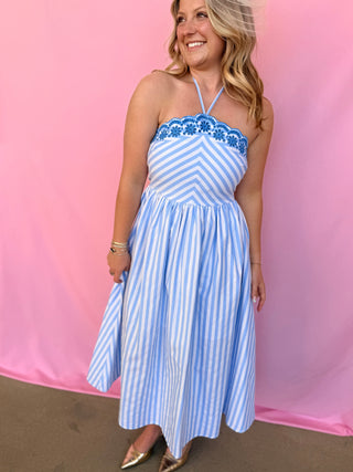 Woman wearing a blue and white striped dress with floral details against a pink background
