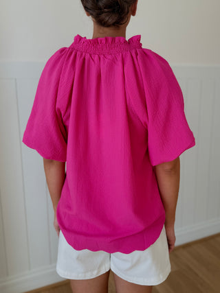 Person wearing a bright pink blouse and white shorts against a plain background