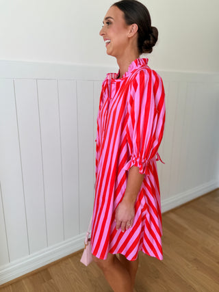 Woman wearing a red and pink striped dress against a white wall.