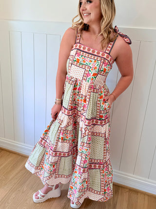 Woman wearing a patterned dress standing against a white paneled wall.