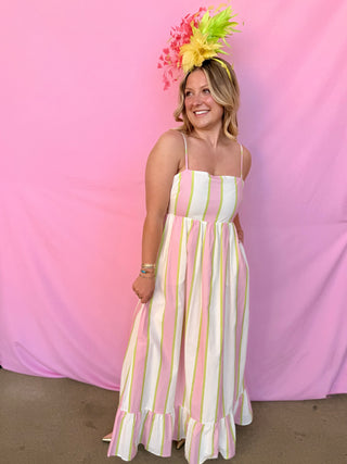 Woman in a striped dress with a colorful headpiece against a pink background