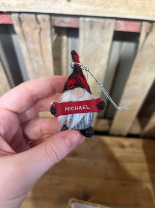Hand holding a small figurine with 'MICHAEL' on a red tag against a wooden background