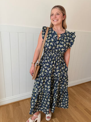 Woman wearing a floral dress standing against a white paneled wall.
