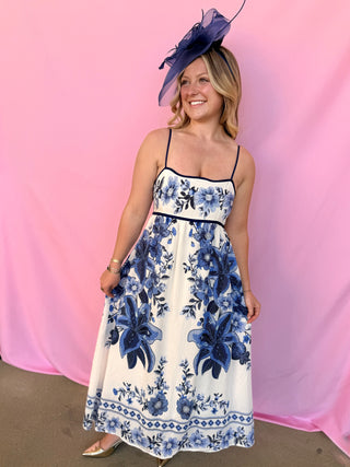 Woman wearing a floral dress with a blue hat against a pink background