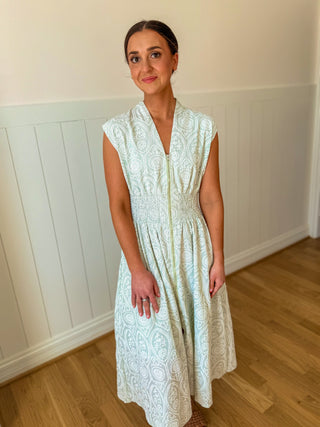 Woman wearing a light green lace dress standing in a room with wooden flooring and white walls.