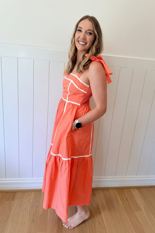 Woman wearing an orange dress with white trim against a white paneled wall.