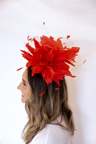 Woman wearing a red feathered headpiece against a white background
