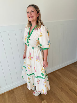Woman wearing a floral dress standing in a room with white walls and wooden flooring.