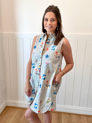 Woman wearing a sleeveless dress with a colorful pattern against a white paneled wall.