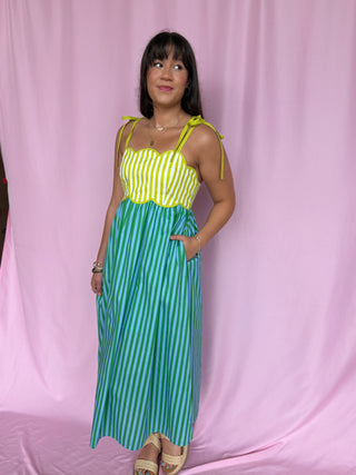 Woman wearing a green and white striped dress with yellow accents against a pink curtain.